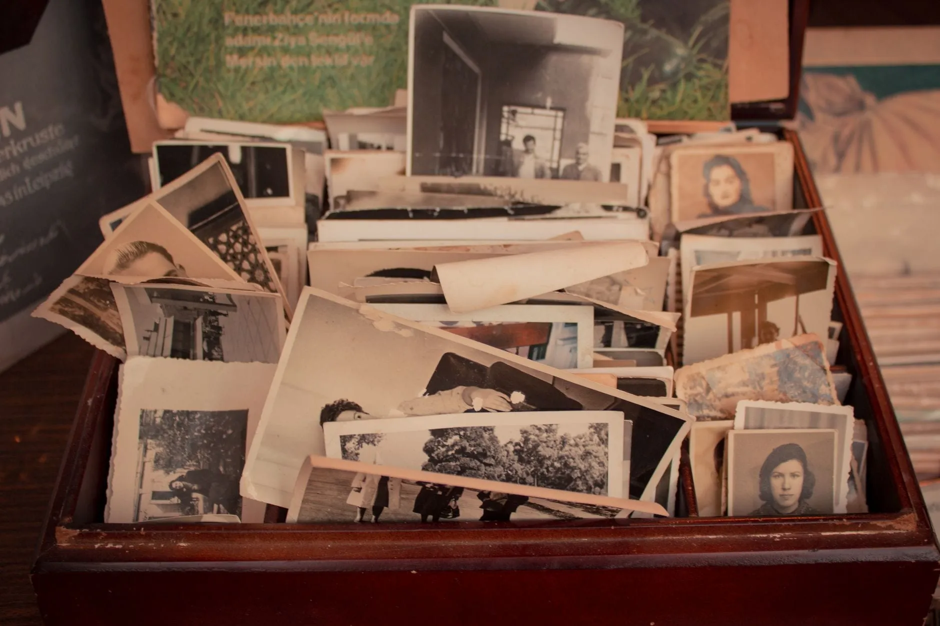 A wooden tray heaped with loose vintage photographic prints of different sizes, some deckle-edged and curling at the corners.
