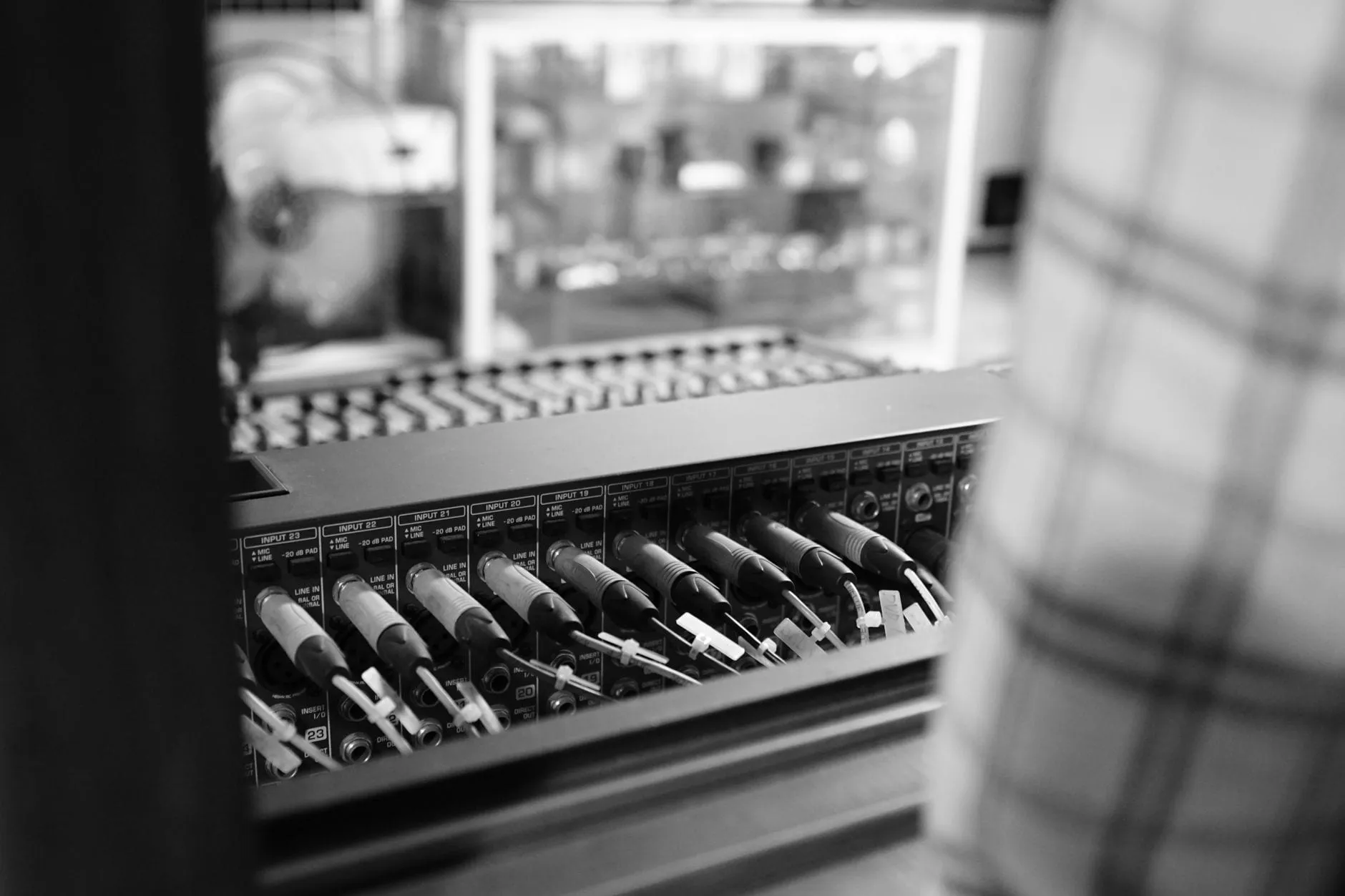 The rear input panel of a mixing desk in black and white, XLR plugs seated in numbered inputs marked MIC/LINE and −20 dB PAD.