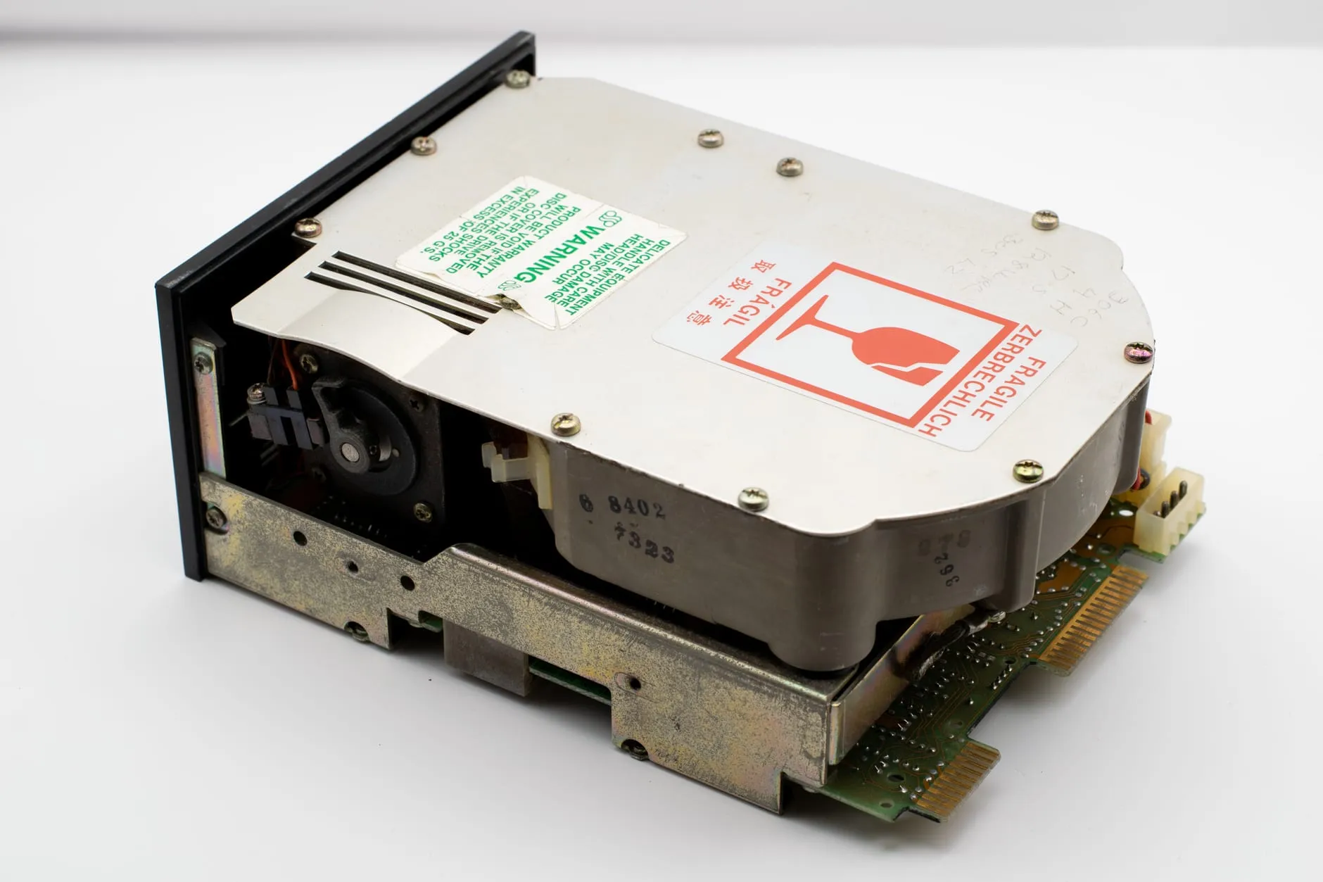 A full-height hard disk drive from the 1980s, its casing marked with a date code and a red FRAGILE sticker in three languages.