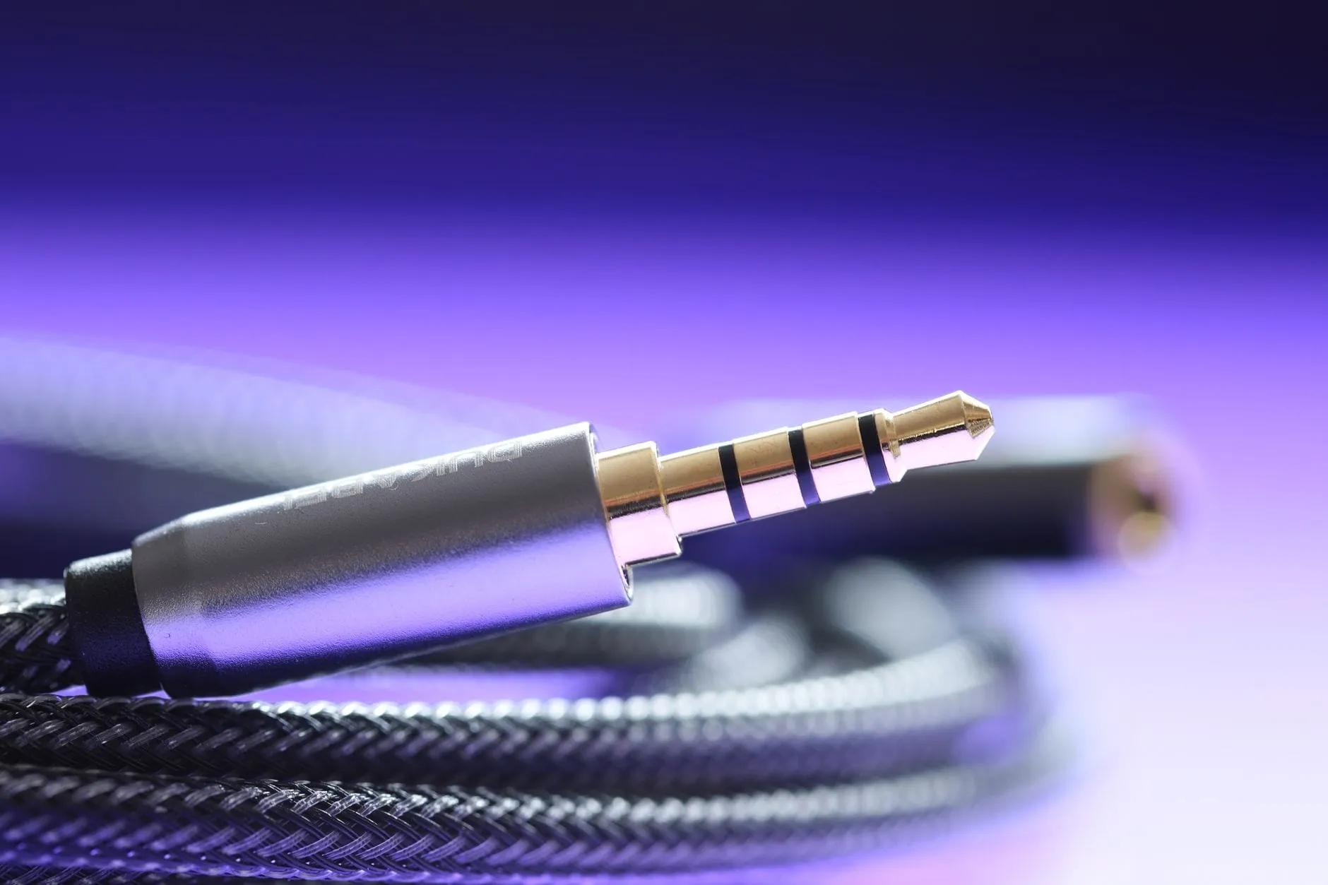 Macro view of a 3.5 mm jack plug on a braided cable, its four gold contact rings clearly separated, lit purple.