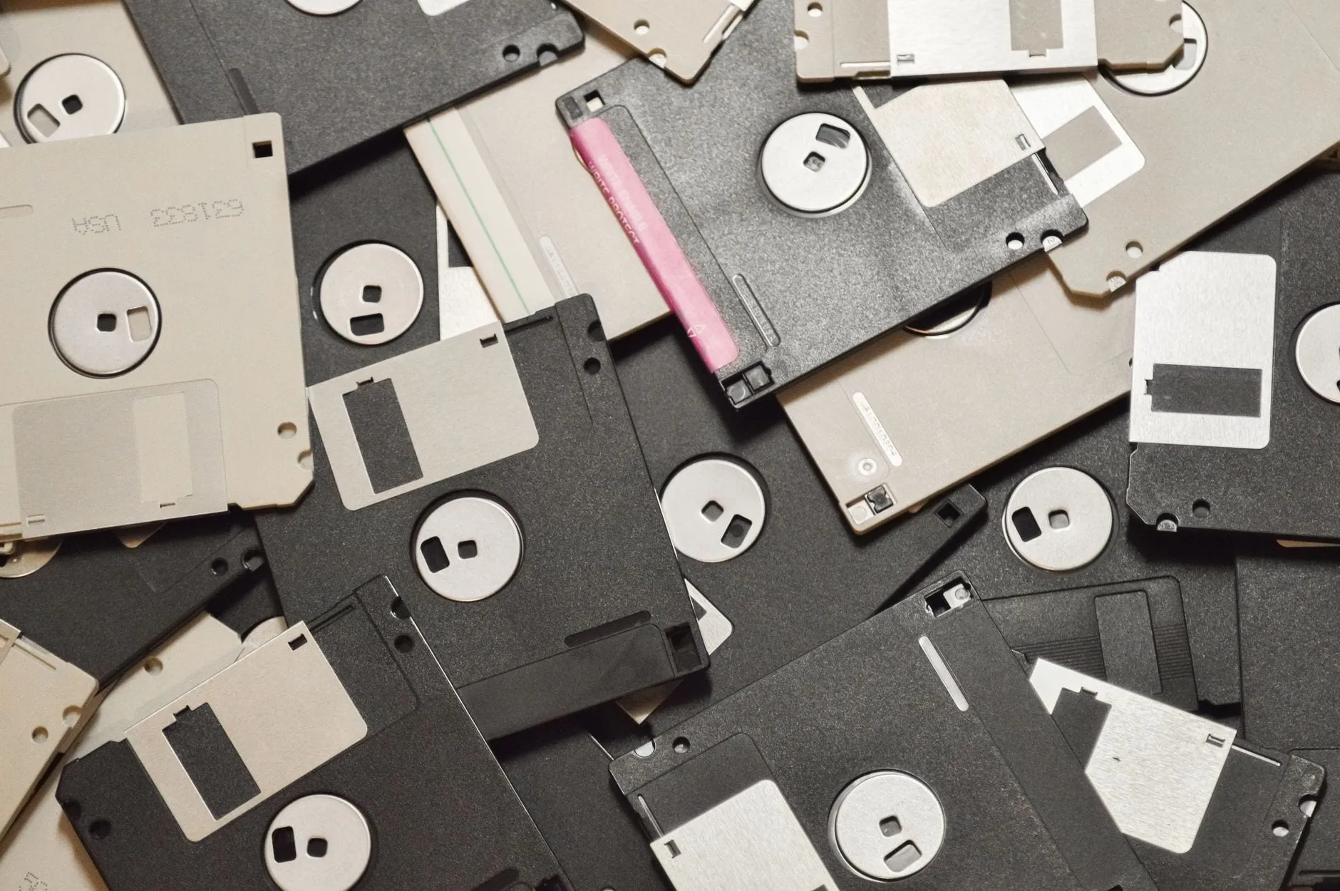 A dense pile of 3.5-inch floppy disks in black and beige plastic, shutters and hub rings visible, photographed from directly above.