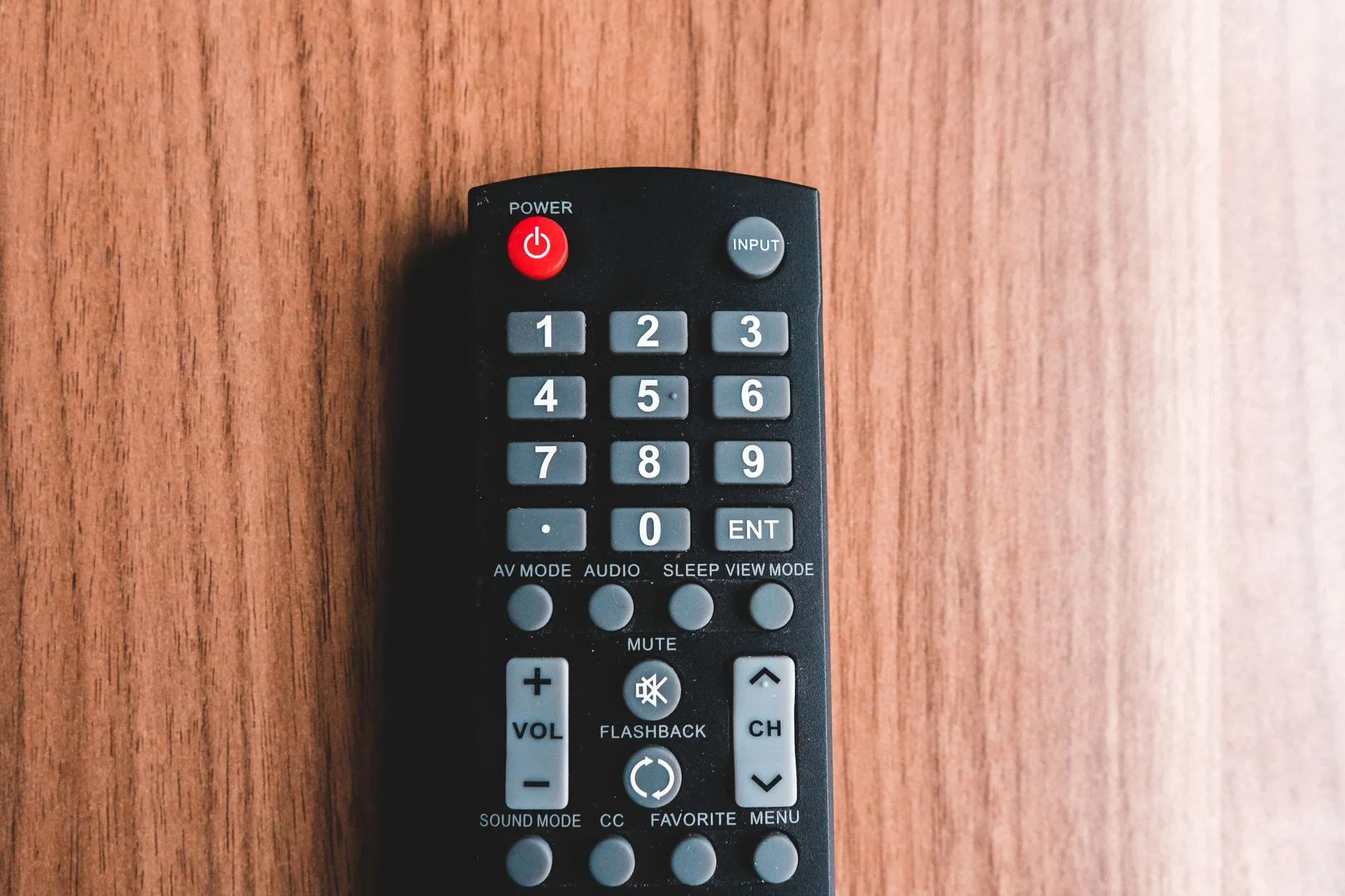 A plain black remote control on a wooden surface, its face crowded with a numeric keypad and buttons labelled AV MODE, SOUND MODE, VIEW MODE and FLASHBACK.