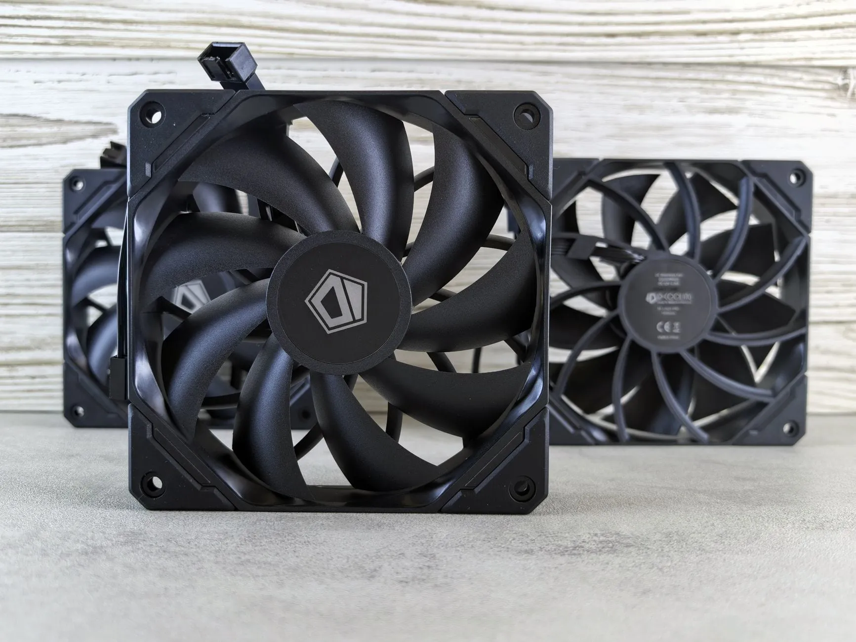 Three black computer case fans standing in a row against a pale wooden background.
