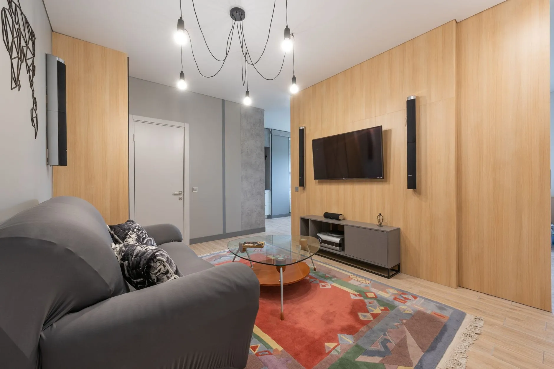 A living room with a wall-mounted television, its screen dark, flanked by tall wall speakers above a low media console.
