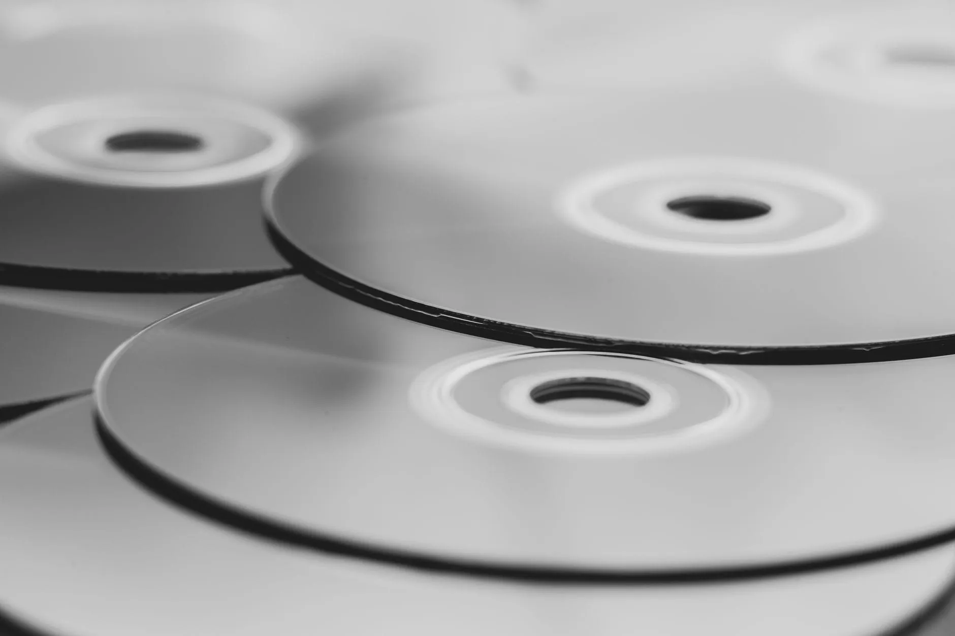 Several unlabelled optical discs overlapping in monochrome close-up, identical to each other apart from where they sit in the pile.
