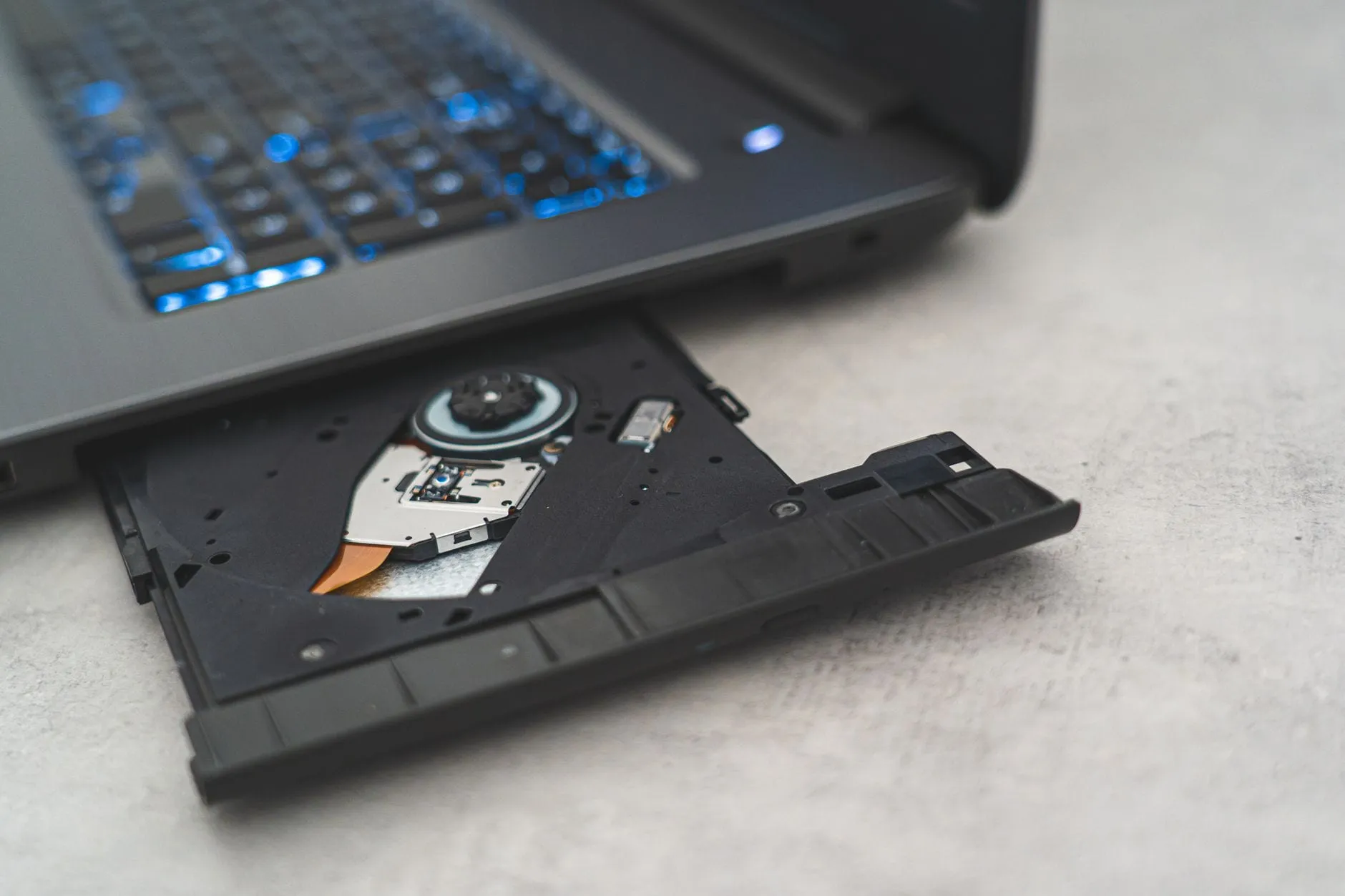 The ejected optical drive tray of a laptop, empty, with the spindle hub and laser assembly visible inside it.