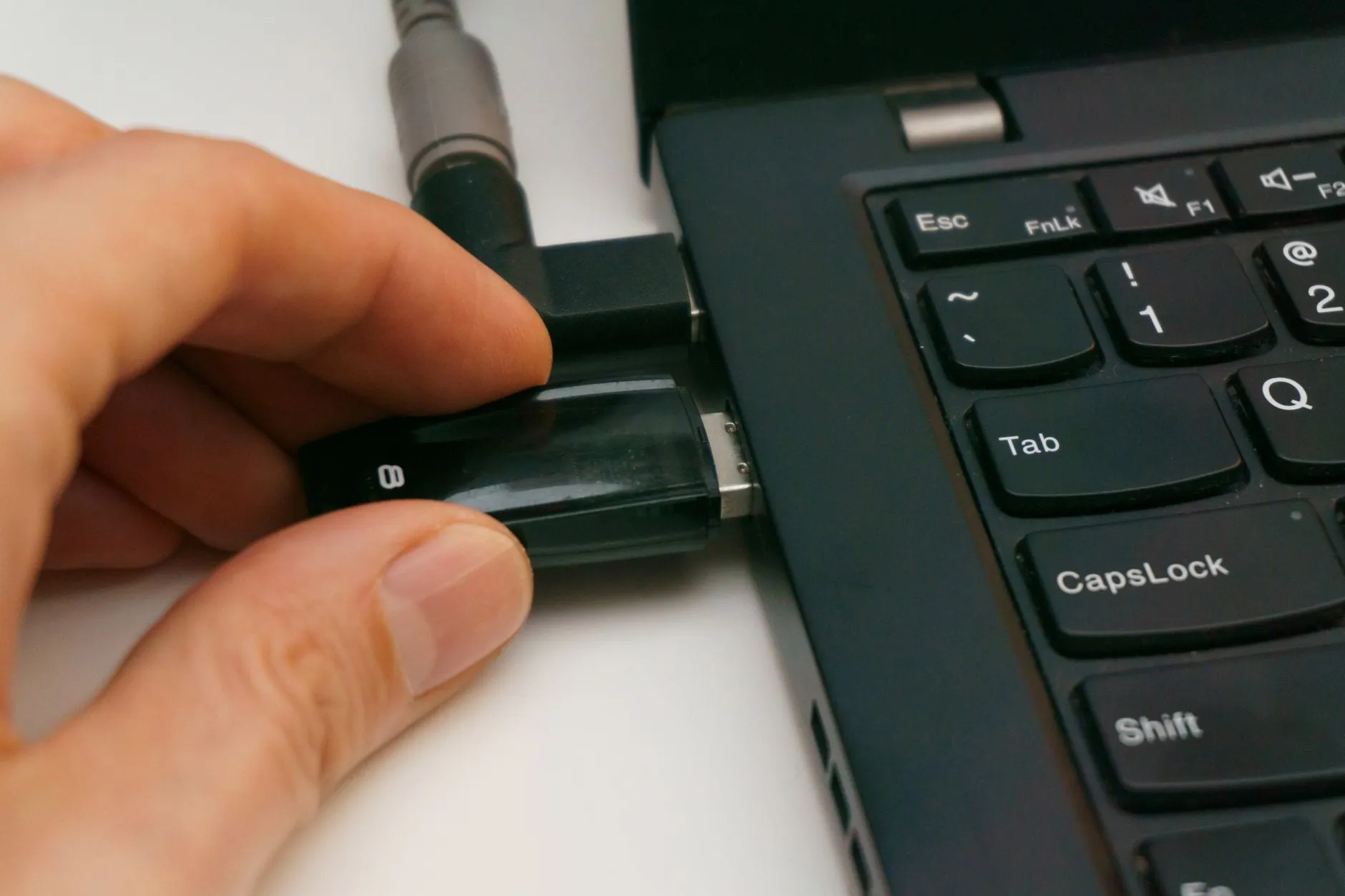 A hand pushing a USB device into a laptop’s side port, beside a second cable already connected.
