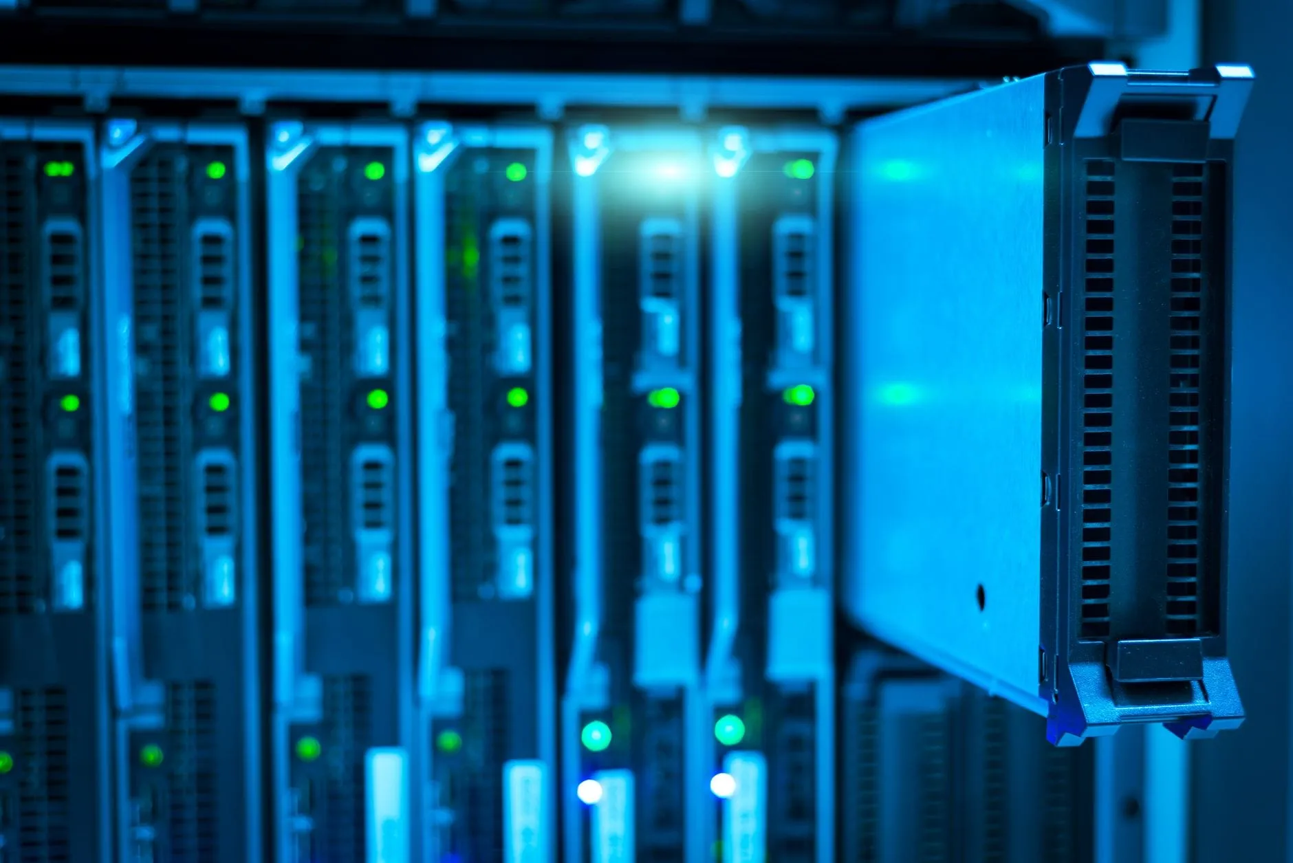 A blade server chassis in blue light with one blade drawn part-way out of its bay, rows of green status lights beside it.