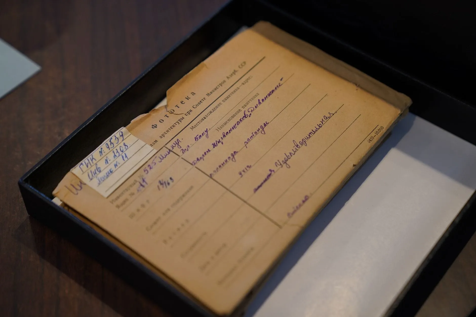An archive folder lying in an open black box, its printed accession form filled in by hand and a pasted label carrying two catalogue numbers.