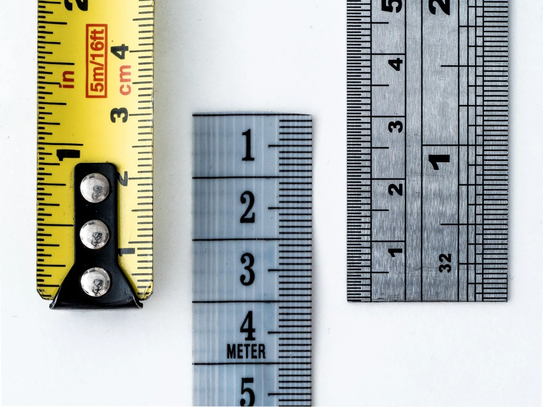 Three measuring scales laid side by side — a yellow tape measure, a metre rule and a steel rule — each divided more finely than the last.