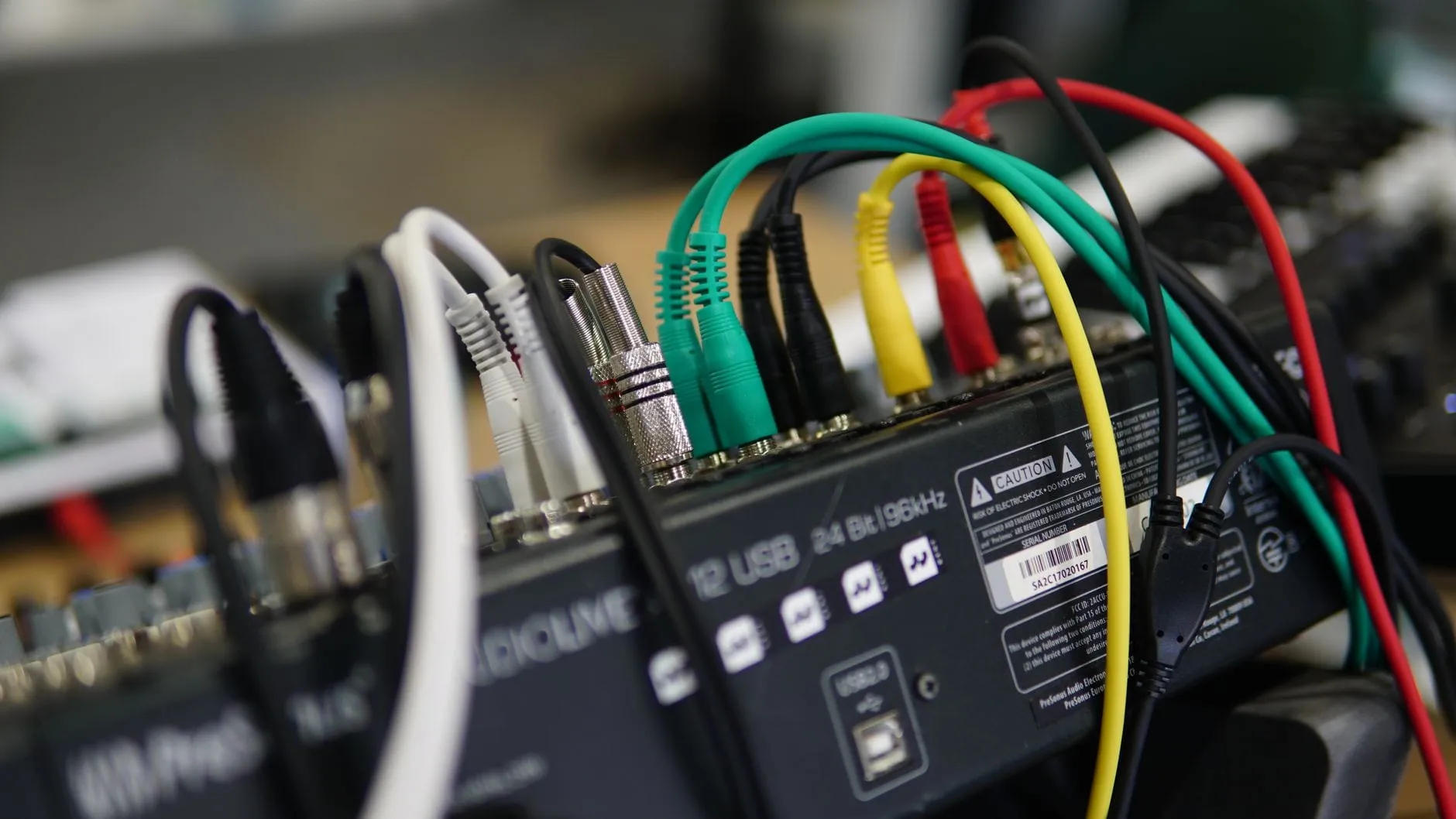 The rear panel of a small audio mixer with green, yellow, red and black patch cables plugged into it, the panel printed 24 Bit | 96kHz.