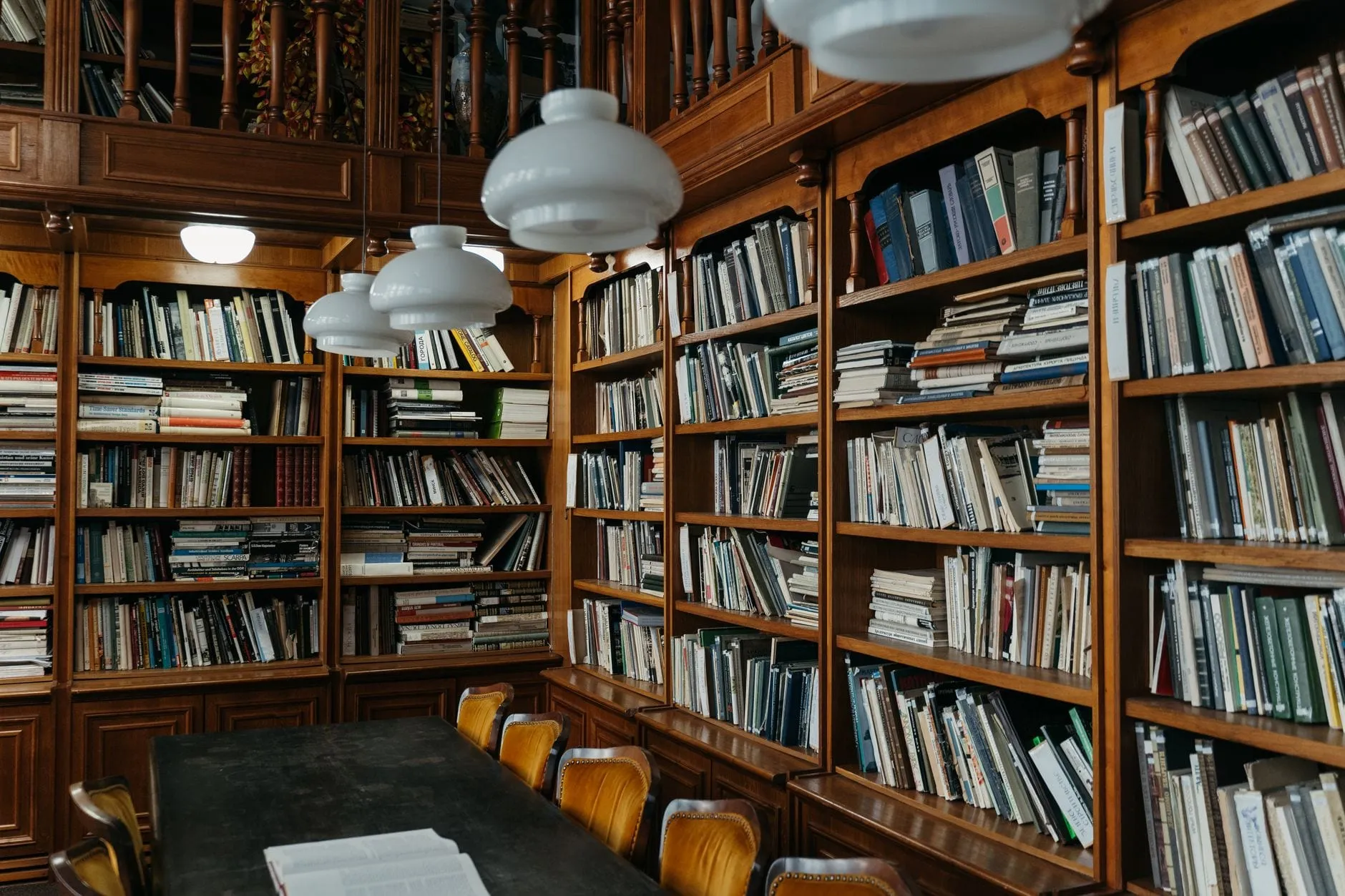 A wood-panelled library reading room, shelves packed with reference volumes on every wall and an open book left on the long table.